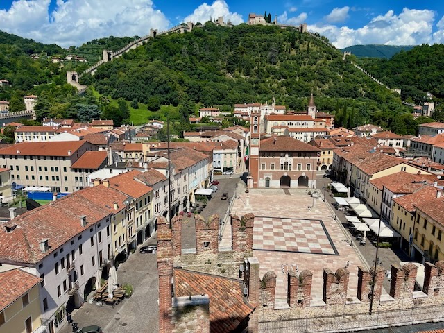 A scenic aerial view of Marostica in Veneto, Italy, highlighting the medieval castle walls, terracotta rooftops, and surrounding lush green hills.