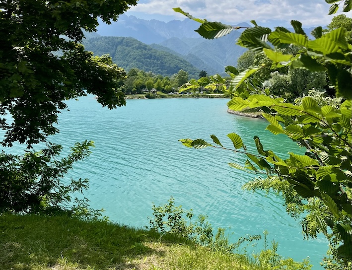 Turquoise waters of Lake Barcis framed by green trees and mountain peaks in Friuli Venezia Giulia.